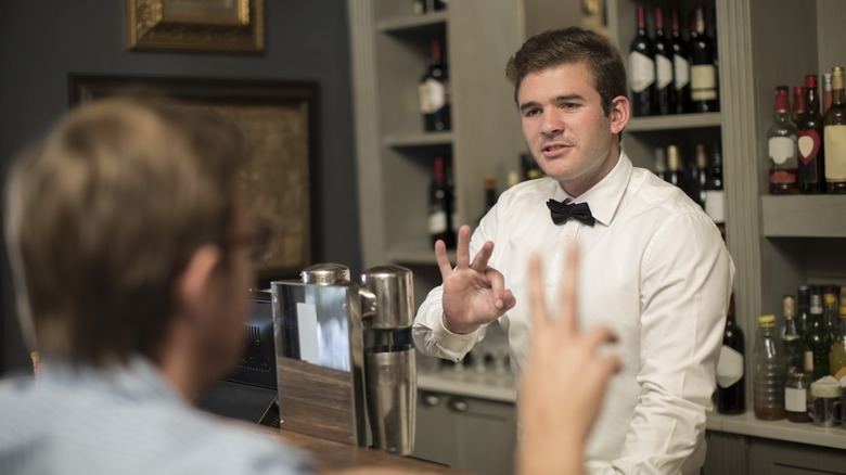 Customer signaling to formally dressed bartender across counter