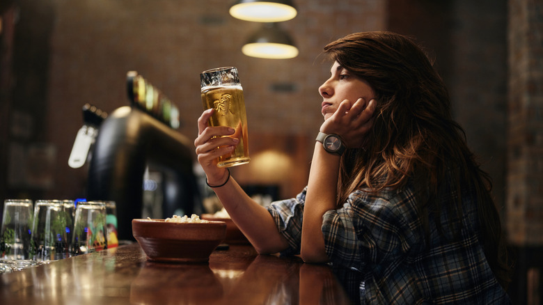 Unamused person staring at beer in hand at bar