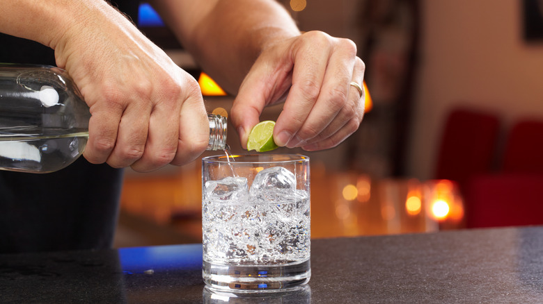 Bartender's hand squeezing lime and pouring vodka into glass