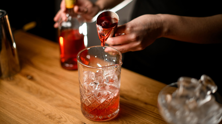 Hands of bartender pouring jigger of liquor into glass