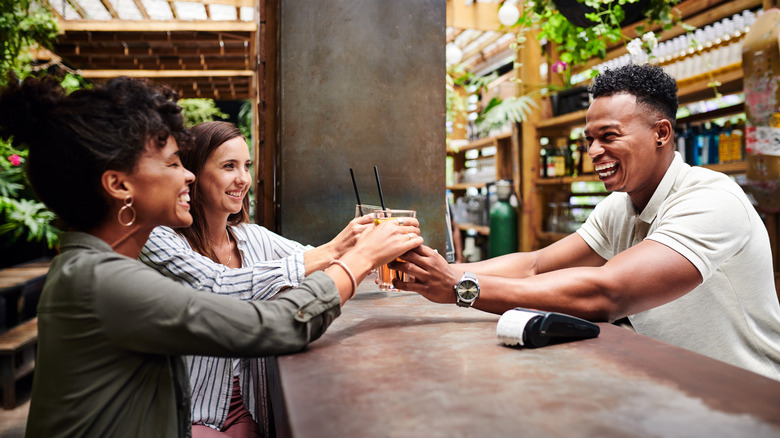 Bartender serving two women drinks over the bar counter