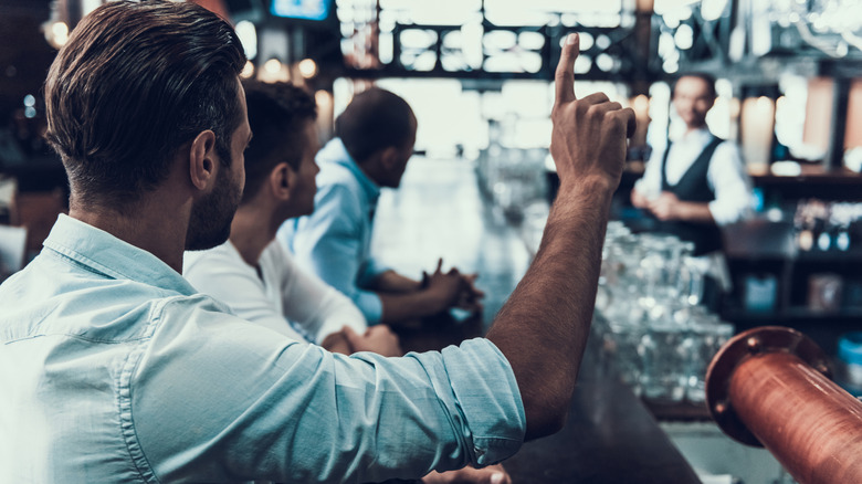 Young man signaling the bartender's attention at a bar