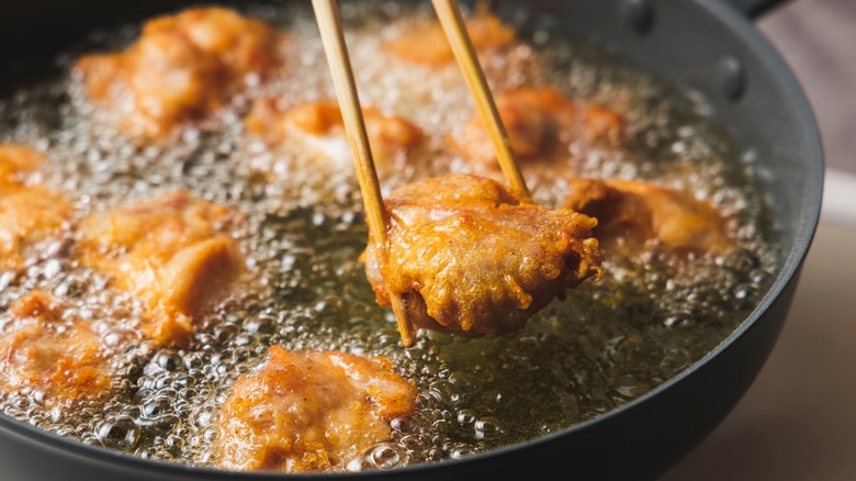 A pair of chopsticks are used to hold chicken in frying oil