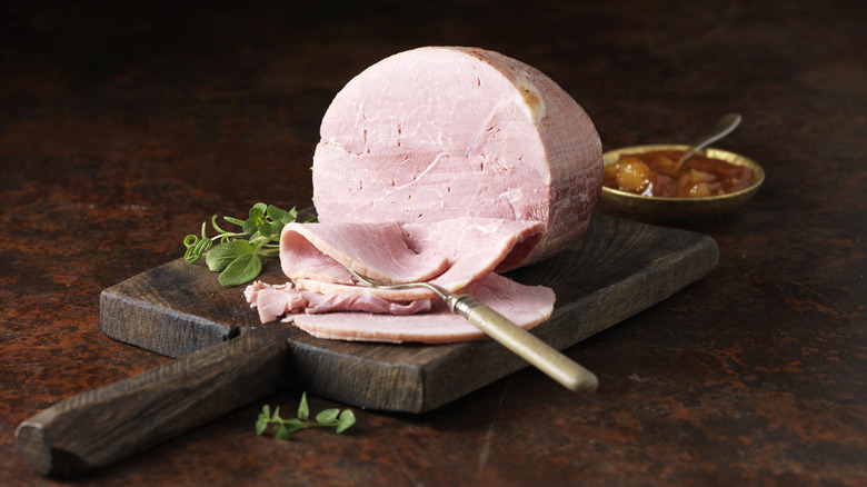 Sliced ham sitting on a wood cutting board next to garnishes and a serving fork