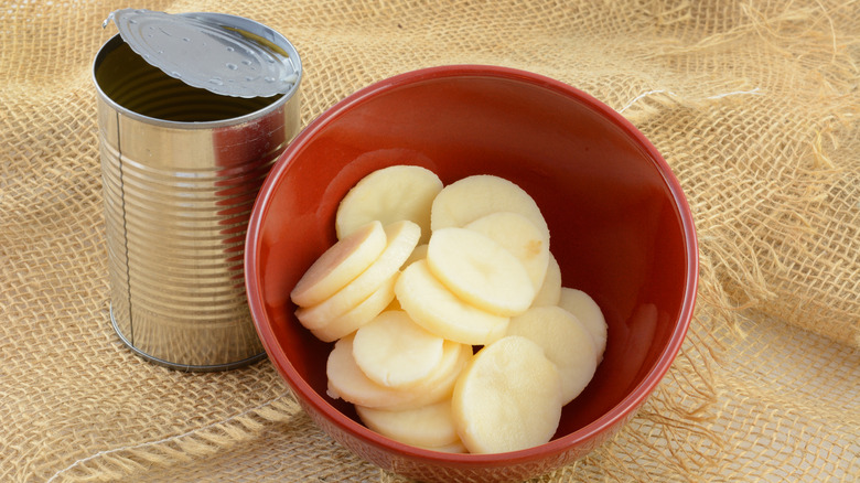 canned, sliced potatoes sit in a red bowl next to opened can on burlap fabric