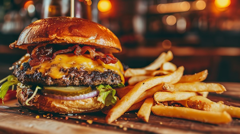 A bacon cheeseburger with fries on a wood cutting board