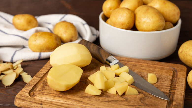 Raw potatoes a wooden cutting board next to a knife