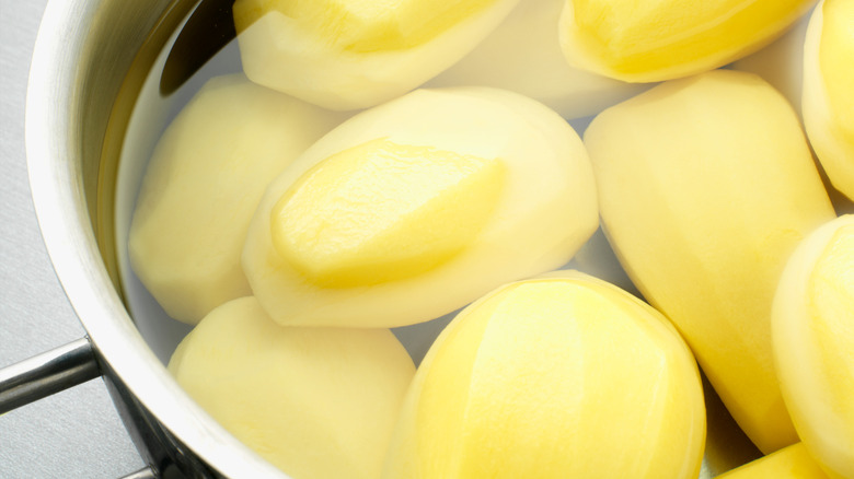 Peeled raw potatoes submerged in a pot of water