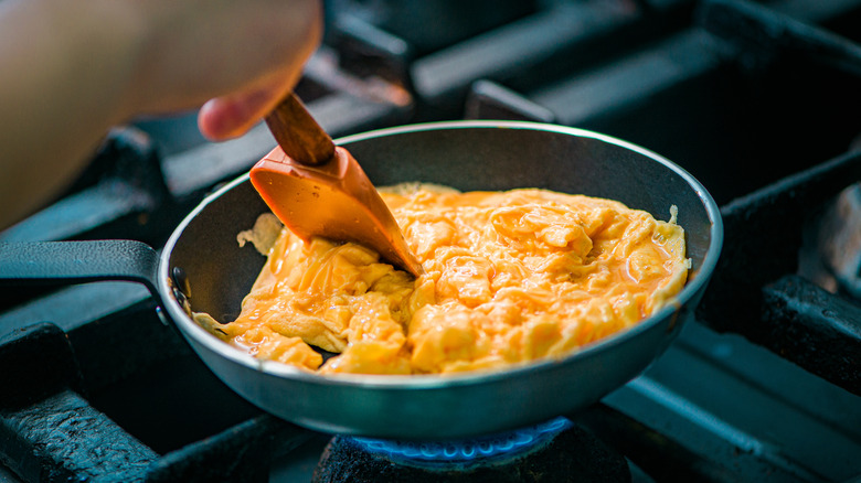 a hand preparing scrambled eggs on a stove