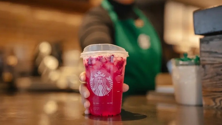 A hand holds a Starbucks cold cup containing a red-colored beverage