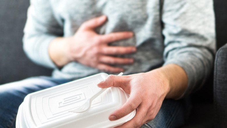 A man holds his stomach with one hand and a takeout container in the other