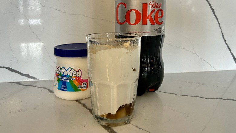 Jar of marshmallow fluff, two liter of Diet Coke, and glass filled with mixture