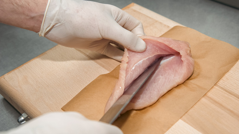 slicing raw chicken breast in half