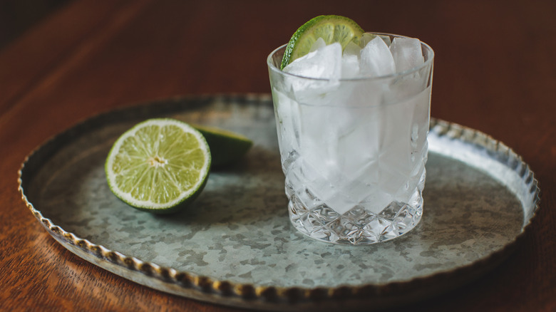 A gin and tonic sitting on a silver tray next to half a lime.