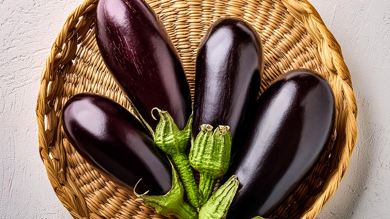 Four eggplants in a wicker basket on a white background.