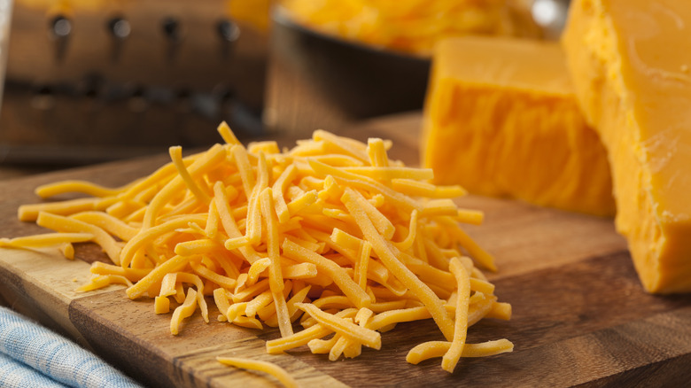 shredded cheddar cheese on a cutting board with blocks of cheddar