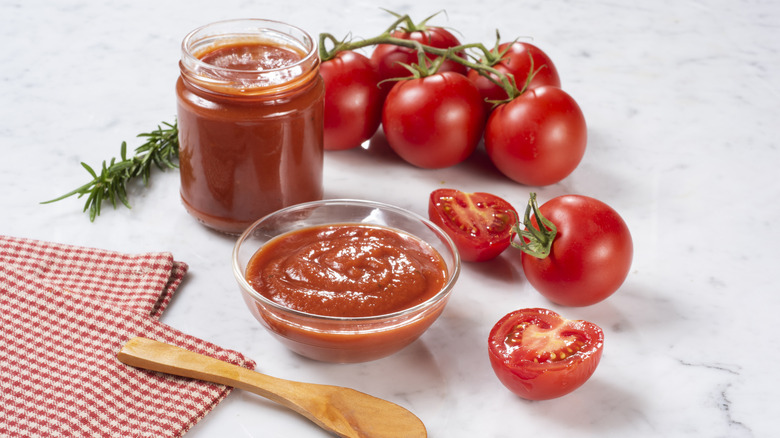 Fresh tomatoes next to a jar and bowl of tomato sauce