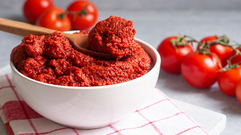 Bowl and spoon of thick tomato paste next to tomatoes