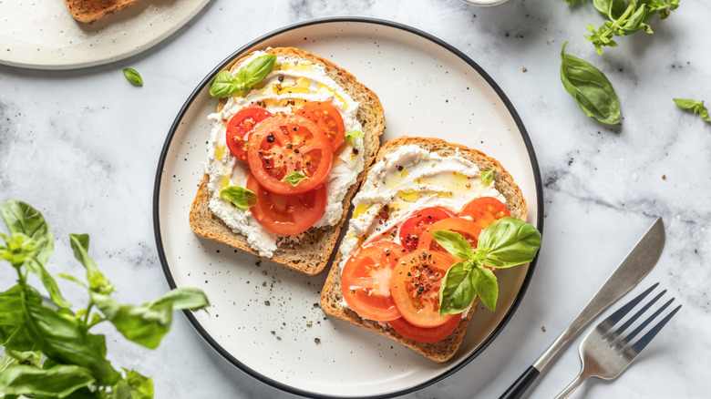 An open face tomato sandwich with hummus and fresh basil