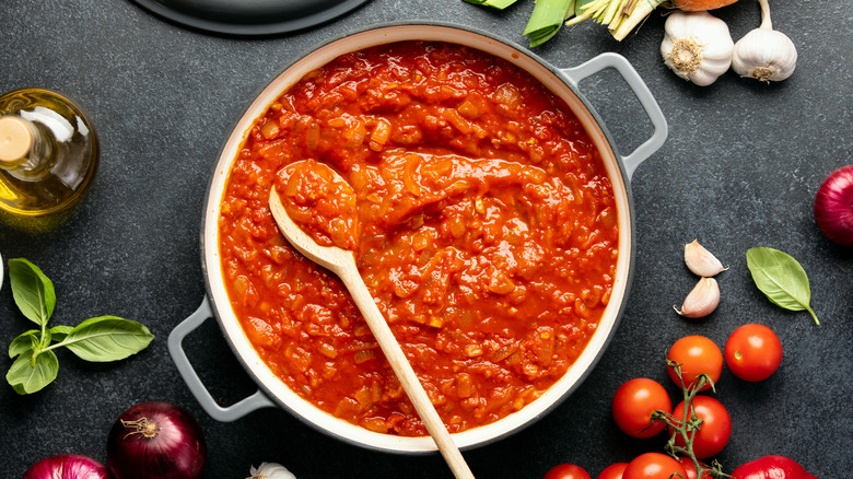 Pan with homemade tomato sauce surrounded by vegetables and herbs