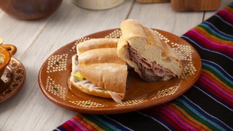 sliced Mexican torta sandwich on plate set atop colorful woven cloth