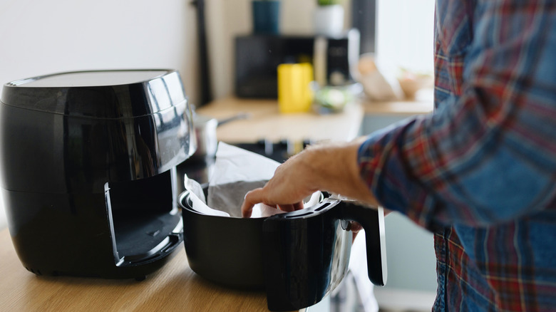 person placing parchment paper into air fryer basket to prepare food