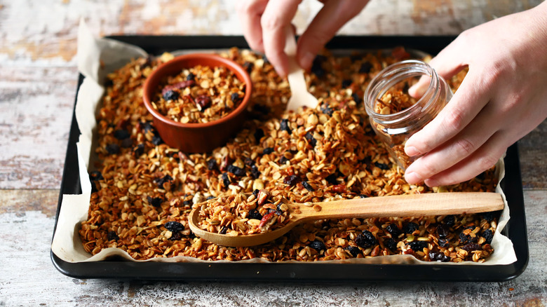 person scooping homemade crispy granola from tray into a jar