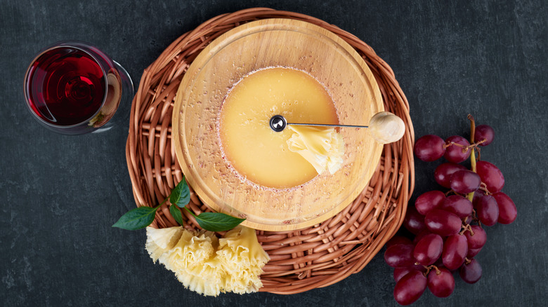 a round of tete de moine cheese with grapes and a glass of wine