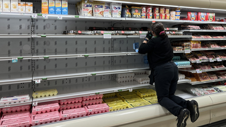 A grocery store employee stocks eggs amid empty shelves