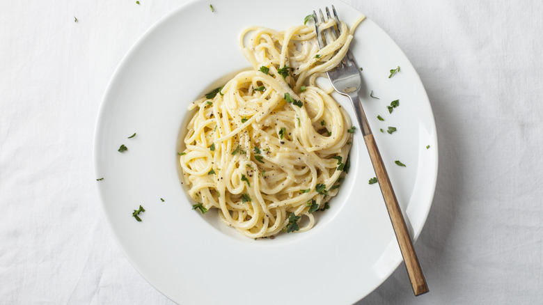 A bowl of pasta with alfredo sauce garnished with some fresh herbs with a fork on the side.