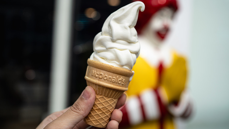 Hand holding a McDonald's vanilla ice cream cone in front of Ronald McDonald