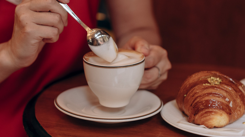 A person stirring a cappuccino with a spoon.