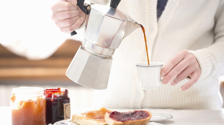 A person pouring espresso from a moka pot into a mug.