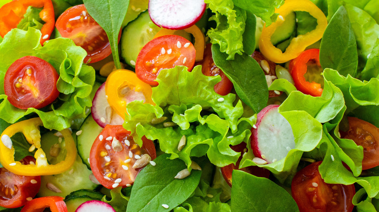 A close up shot of a salad with a variety of vegetables including cucumbers, radishes, and tomatoes