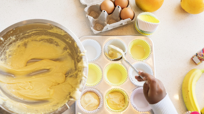 Person's hand spooning cake batter into a muffin tray