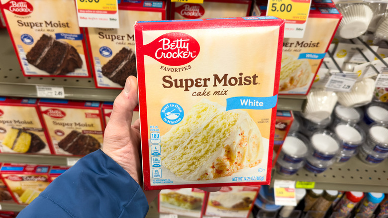 Person's hand holding a box of cake mix in a grocery store