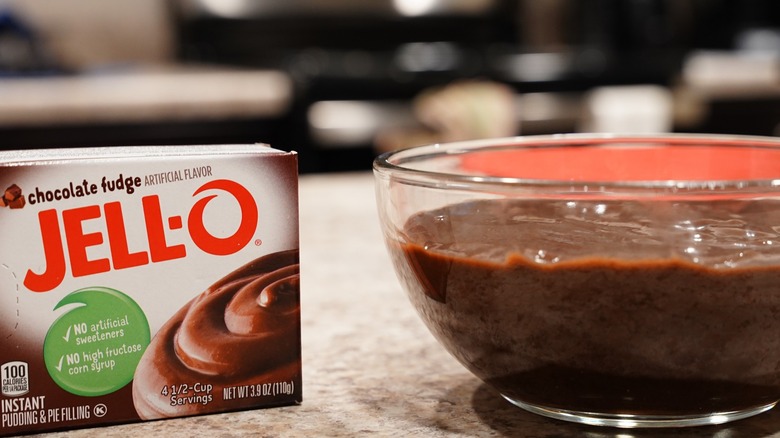 A box of chocolate flavored Jello pudding with a bowl of it to its right.