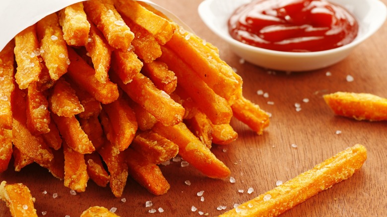 Container of crispy sweet potato fries next to a bowl of ketchup.