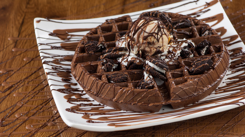 A chocolate brownie waffle topped with ice cream, oreo cookies, and chocolate sauve