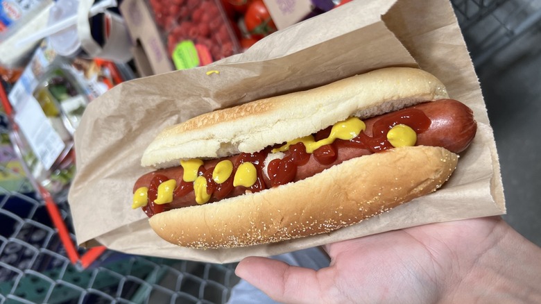 a costco hot dog with ketchup and mustard on an outstretched hand