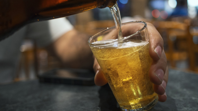 A person pouring a bottled beer into a small glass