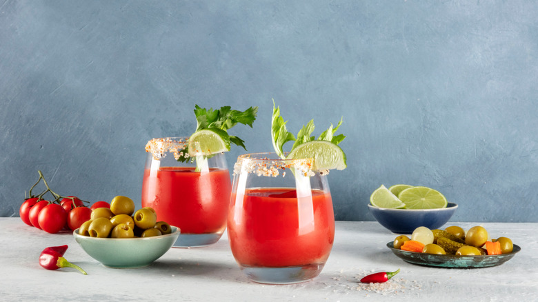 Two red cocktails with various garnishes around glasses