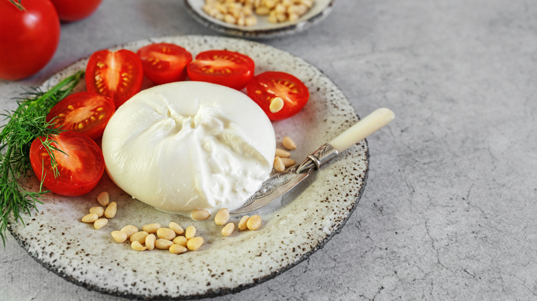 Creamy burrata on a plate with tomatoes and pine nuts