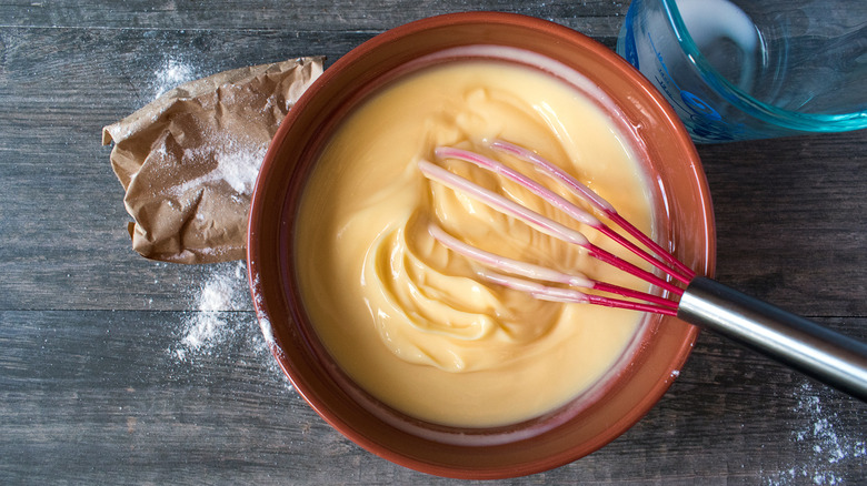 Bowl of vanilla pudding with a whisk, a bag of flour and empty measuring cup