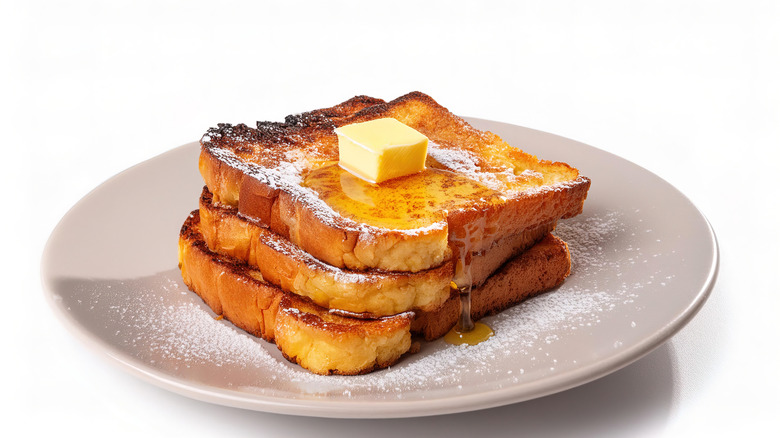 Stack of French toast on a white plate with butter on top