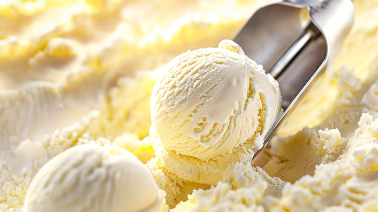 An ice cream scoop lifts one of two scoops of vanilla ice cream