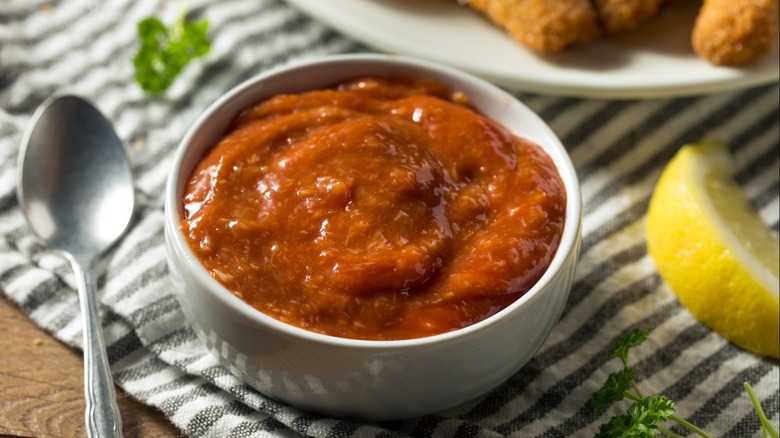 small bowl of cocktail sauce near a spoon and lemon wedge