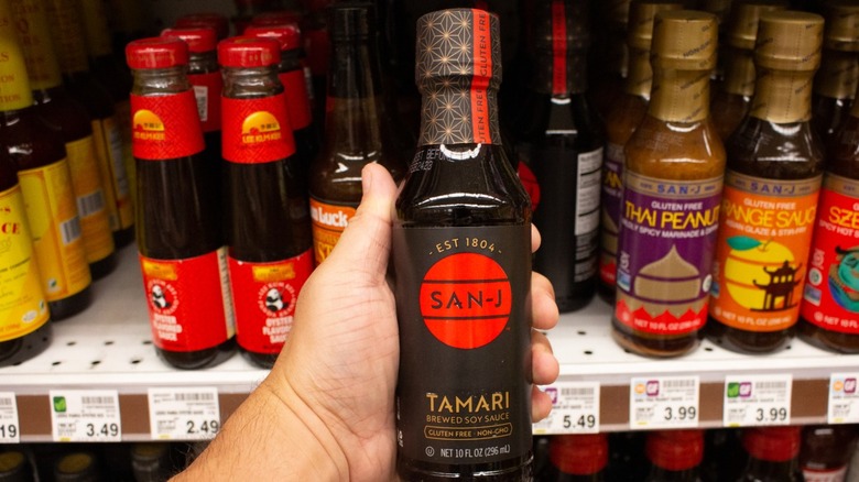 Bottled tamari sauce held up by other asian sauces in grocery store