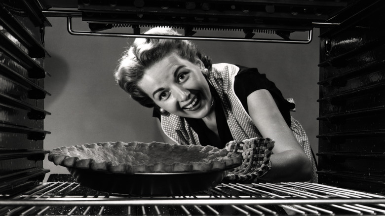 black and white photo of a woman putting a pie crust in the oven