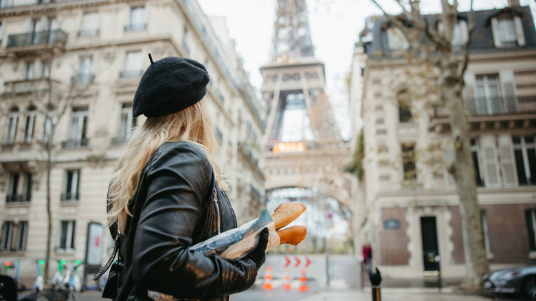 a woman carries two baguettes in front of the Eiffel Tower in Paris